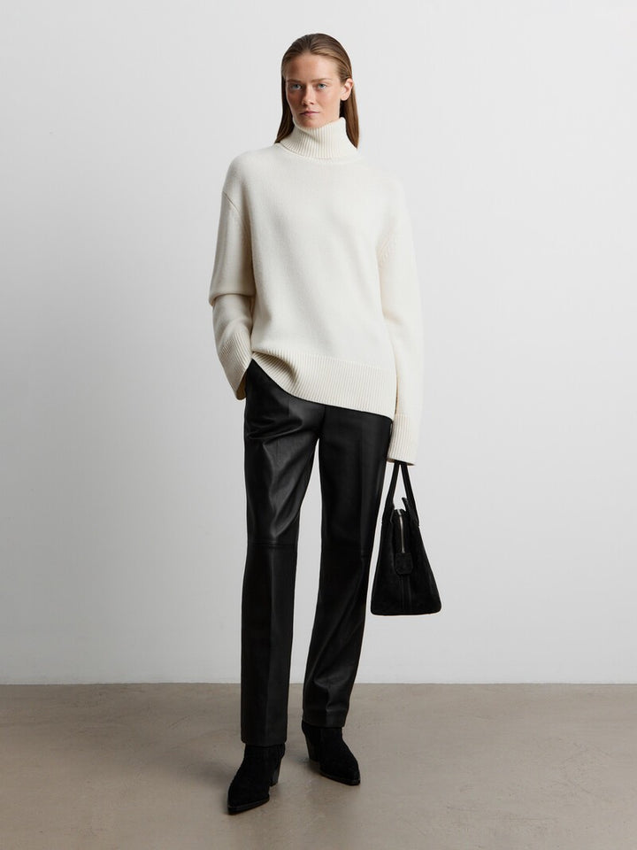 Cream turtleneck sweater with black leather pants and ankle boots