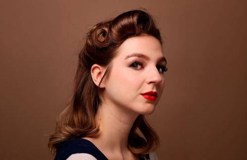 Single portrait of a woman with double victory rolls and red lipstick, chestnut-brown hair.