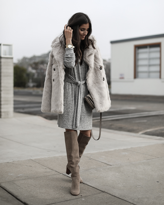 Woman wearing a grey faux-fur coat over a grey knit dress with taupe knee-high boots