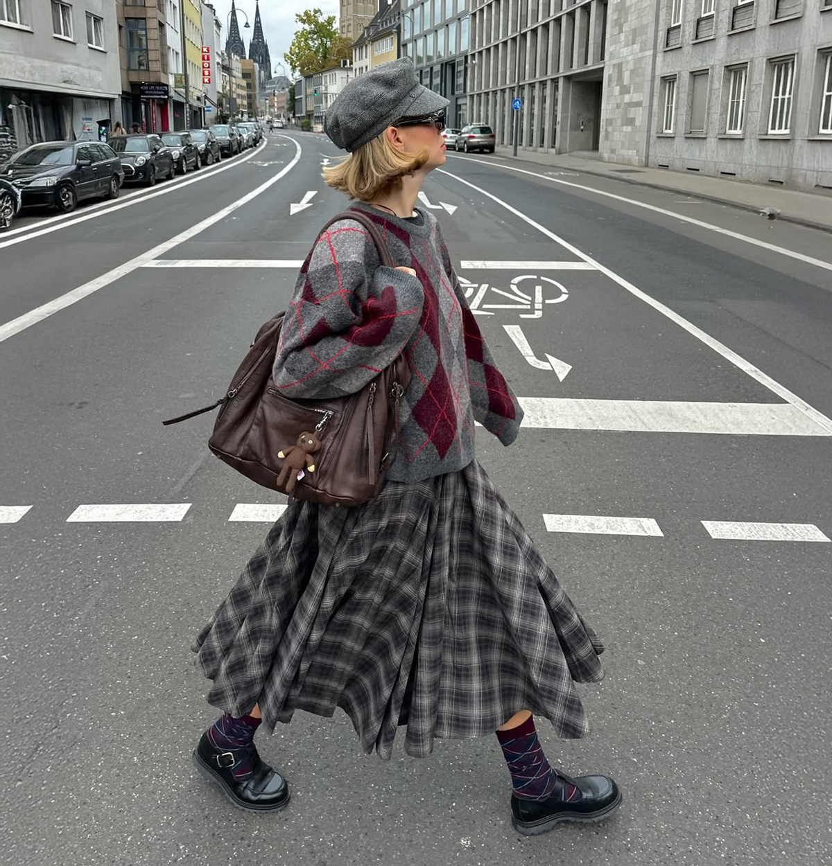 Woman wearing a burgundy argyle sweater with a plaid midi skirt and Mary Jane shoes