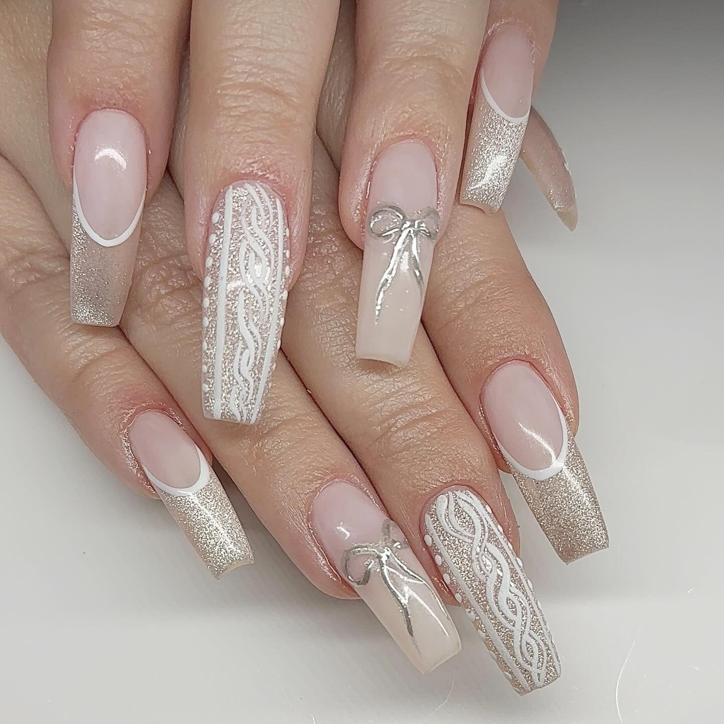 Long coffin nails in champagne glitter with white cable-knit pattern and silver hand-painted bows