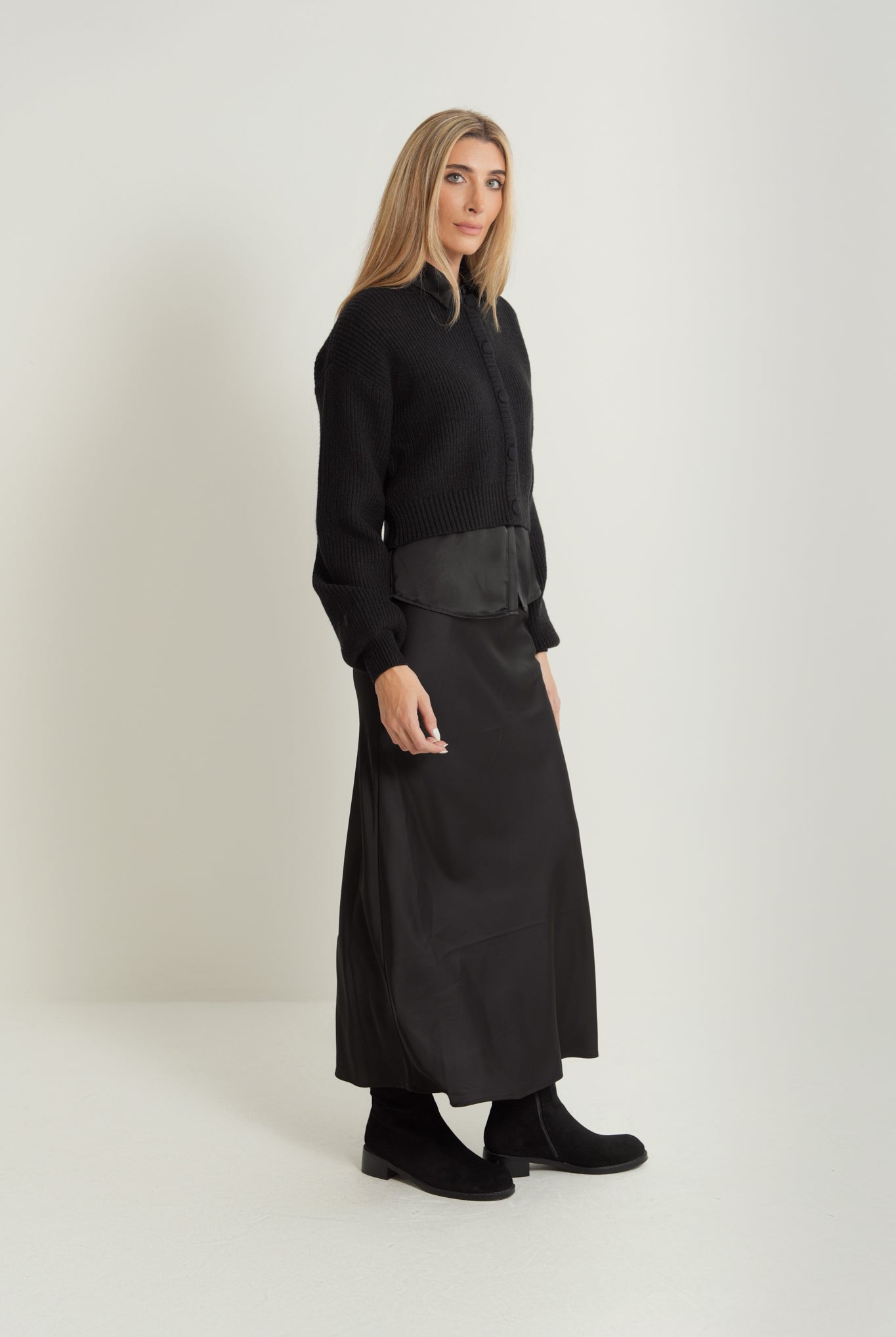 Woman wearing a black satin maxi skirt, black knit cardigan and black Chelsea boots