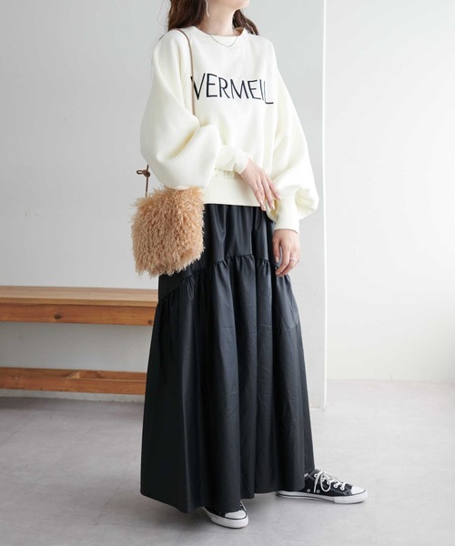 Woman in a cream logo sweatshirt, black faux-leather tiered maxi skirt and black sneakers with a shearling bag