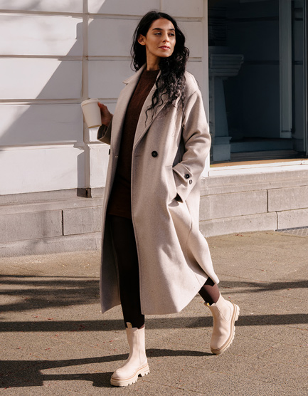 Woman in a beige long coat, brown turtleneck and trousers with cream Chelsea boots