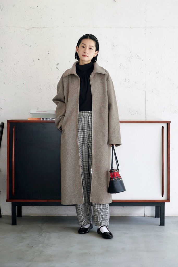 Woman wearing a long taupe wool coat over a black turtleneck and houndstooth check trousers with Mary Jane shoes