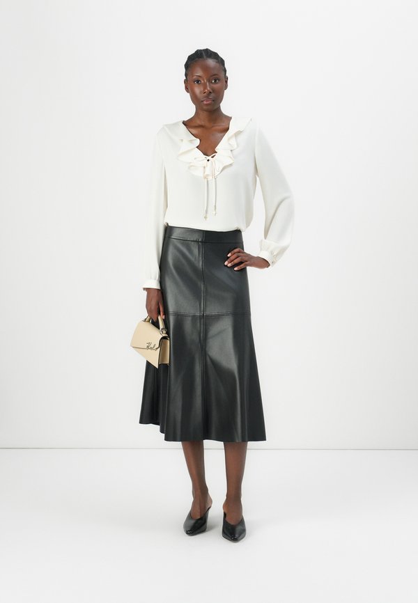 Model in black leather midi skirt with white ruffled blouse and heels