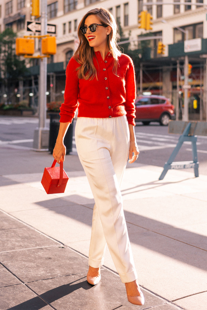 Woman wearing a cherry red cropped cardigan with white wide-leg trousers, nude heels and a red mini bag on a city street