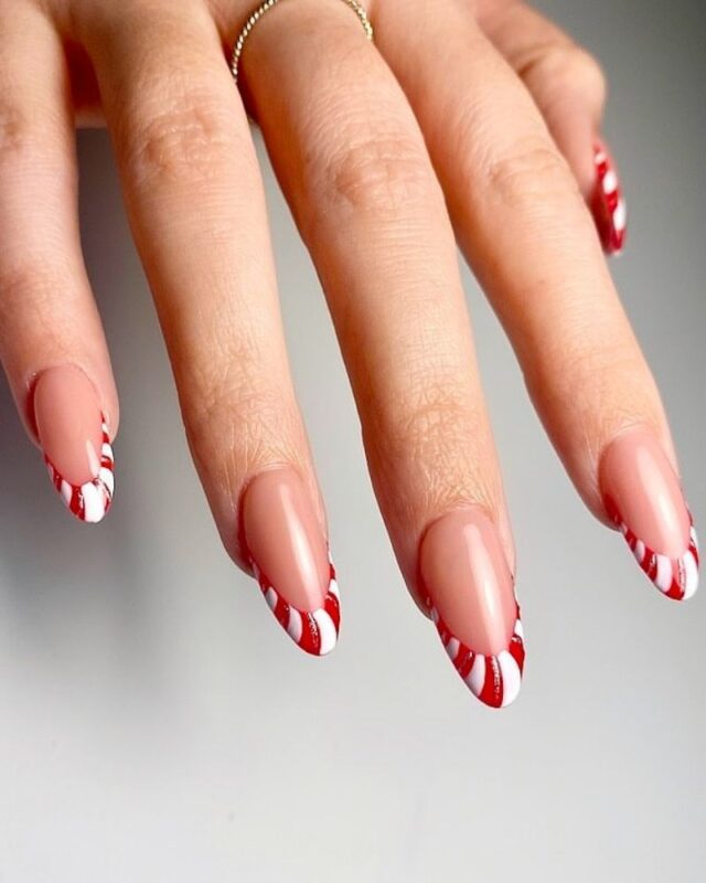 Nude almond nails with French-style tips painted in diagonal red-and-white candy-cane stripes.