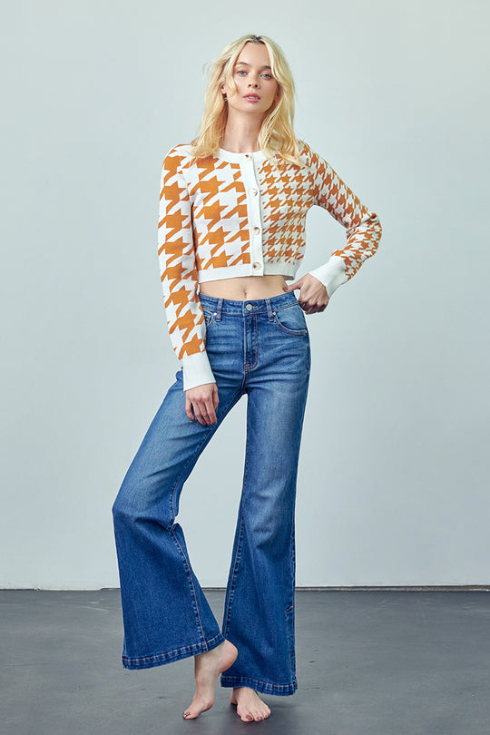 Woman wearing an orange and white houndstooth cropped cardigan with medium-wash flare jeans