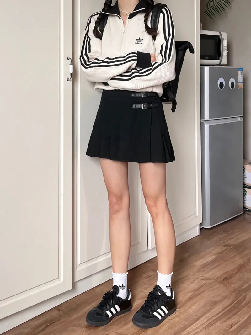 White and black striped track jacket with black pleated skort and black sneakers