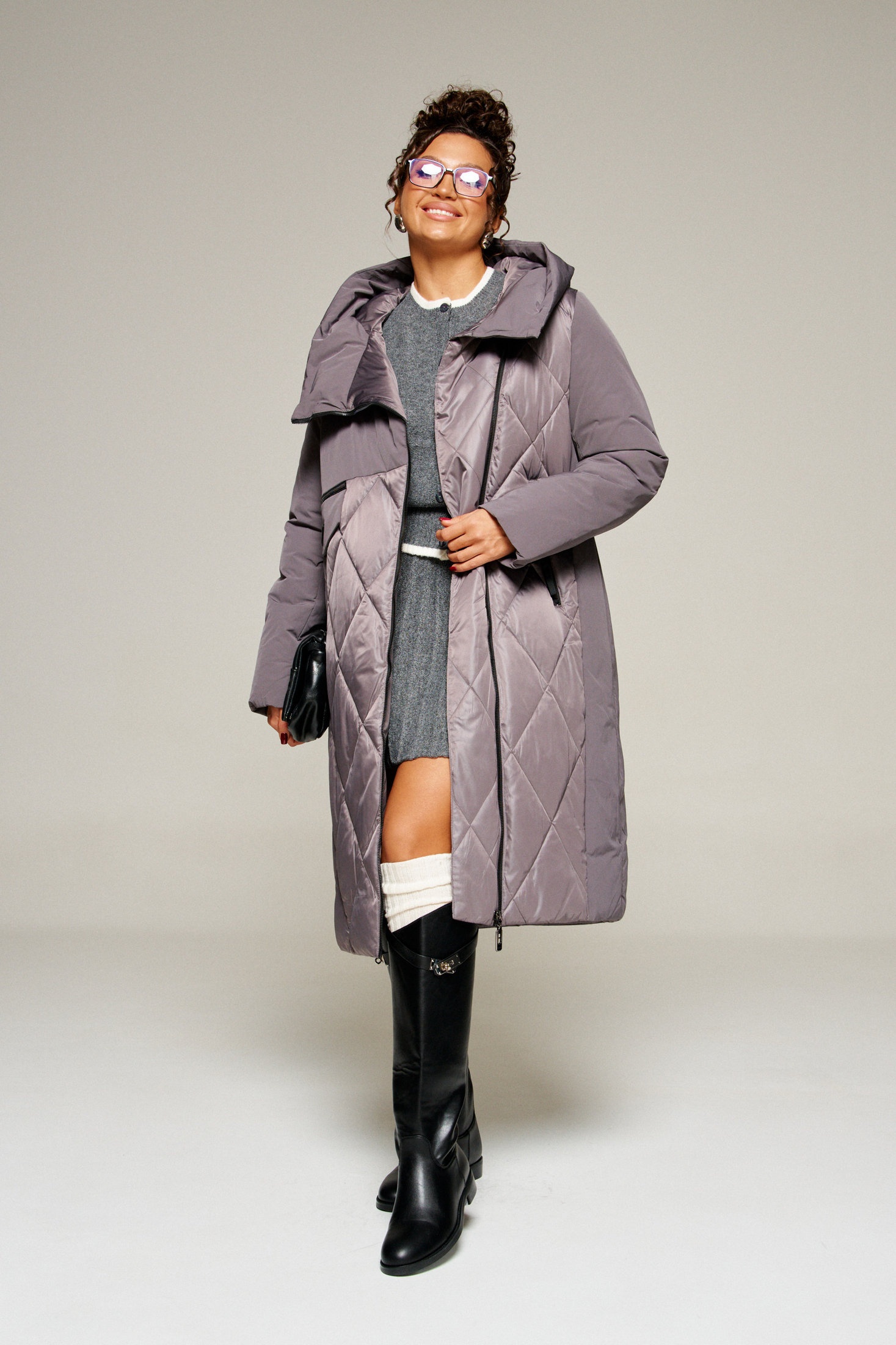 Woman in a mauve quilted long coat over a grey knit set with white socks and black knee-high boots