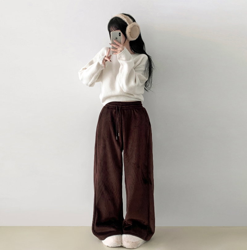 Woman in beige knit earmuffs, white sweater, and brown corduroy wide-leg trousers taking a mirror selfie