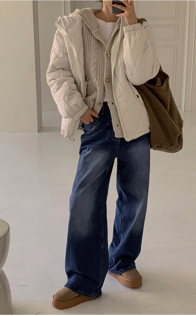 Woman in a white quilted hooded jacket over a cable-knit cardigan with wide-leg jeans and platform boots