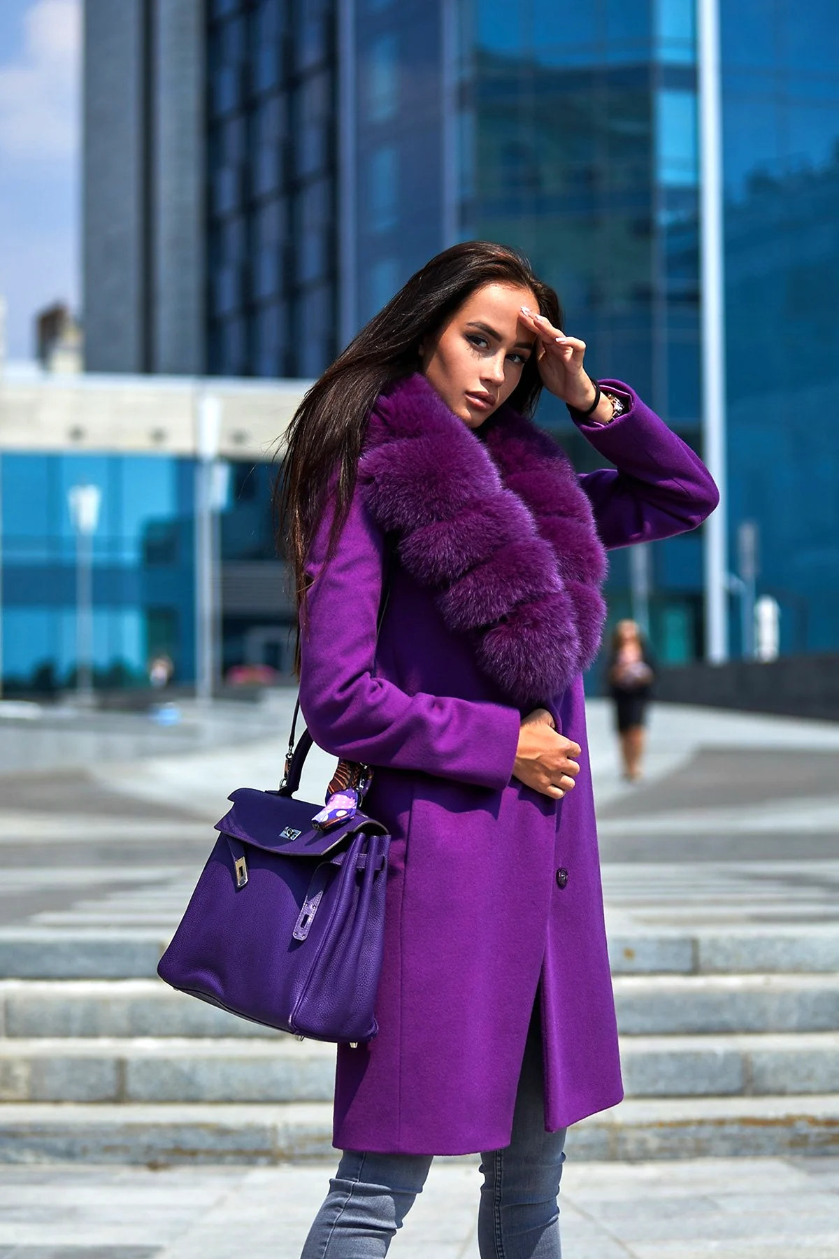 Woman in a dark purple oversized wool coat with feather trim and quilted chain bag