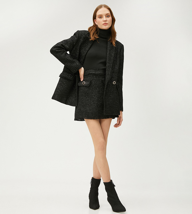 Woman wearing a black tweed blazer, black turtleneck, black tweed mini skirt and black knit ankle boots