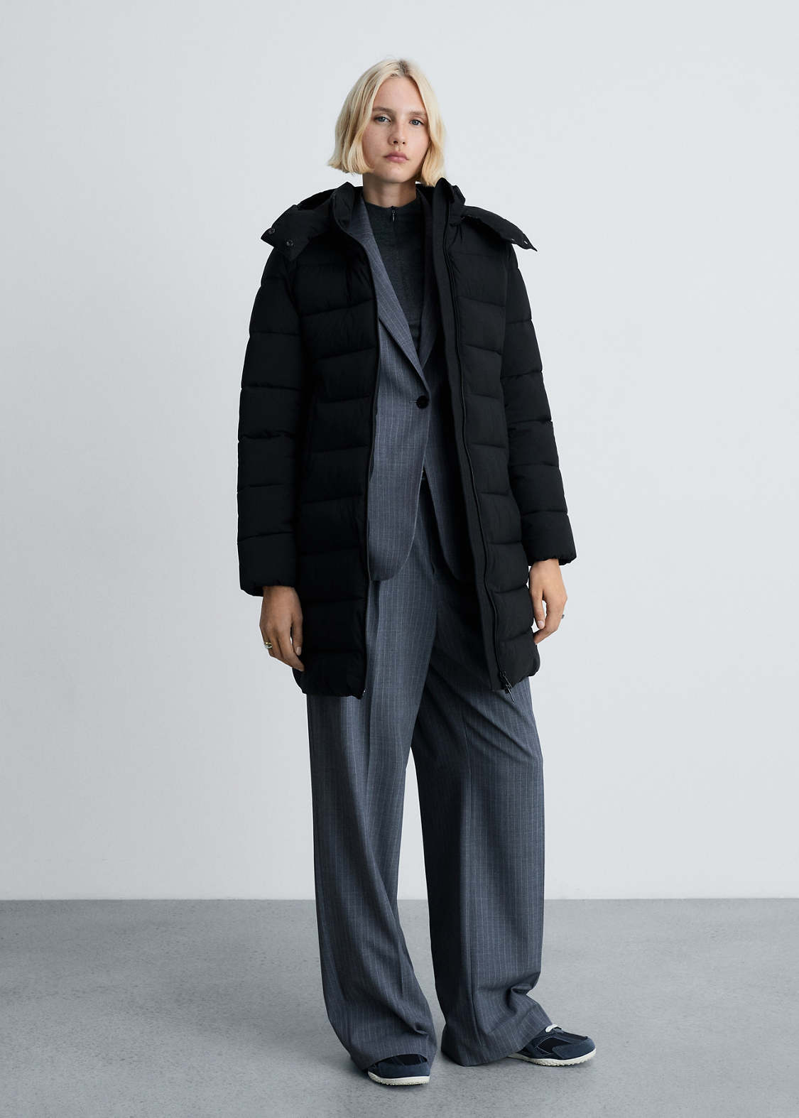 A woman wearing a matte black long puffer coat with a blazer and tapered pants