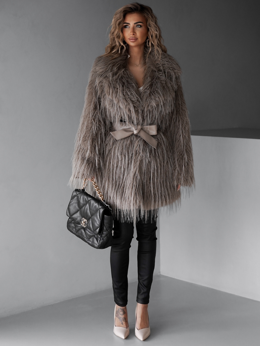 Woman in a faux-fur coat over a satin camisole and black trousers with heels