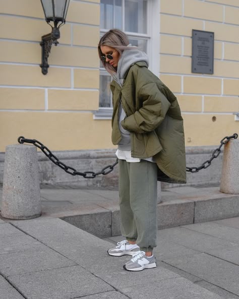 Woman in olive cargo joggers, gray hoodie, olive puffer and white sneakers on a city street