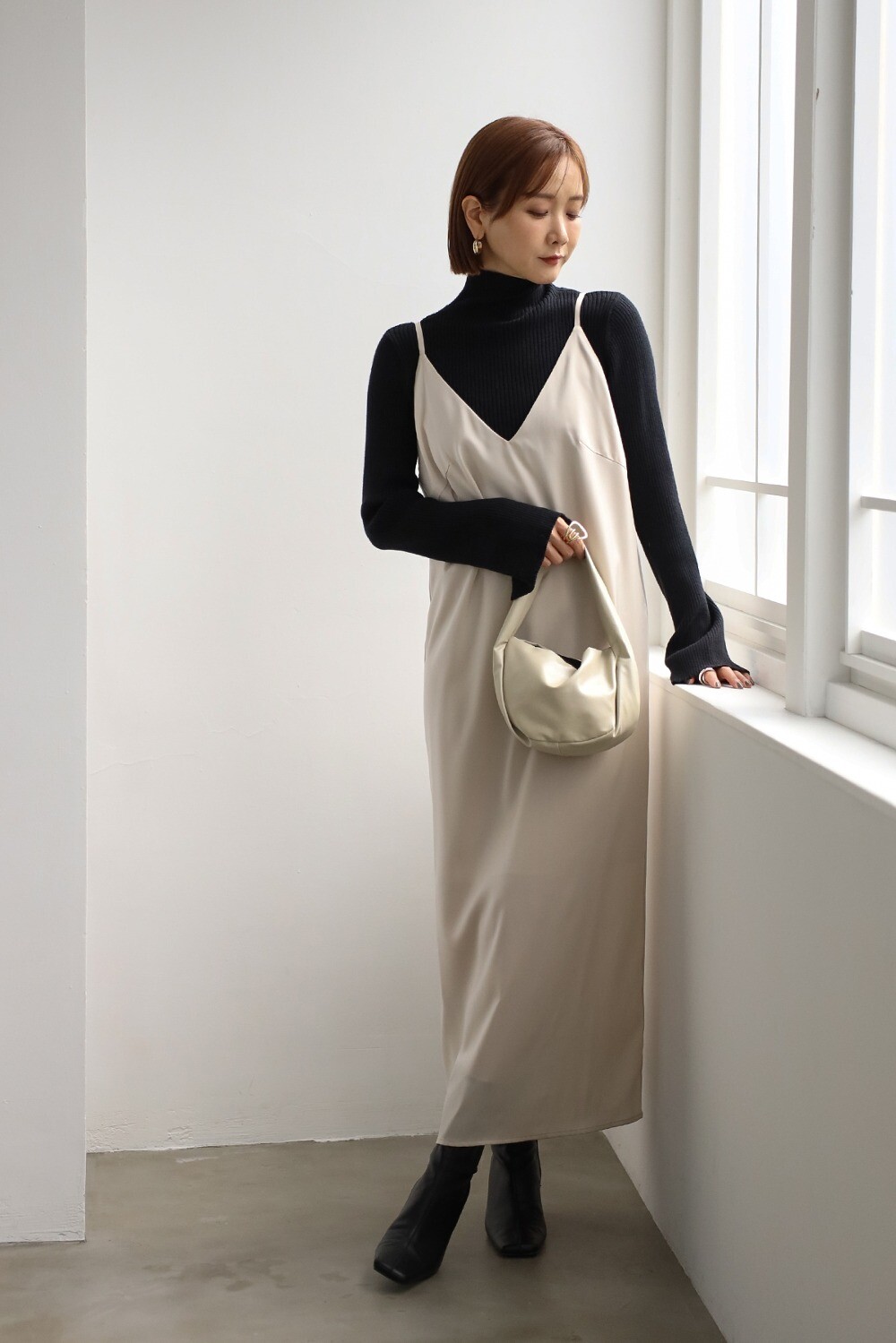 Woman layering a black turtleneck under a champagne satin slip dress with black boots