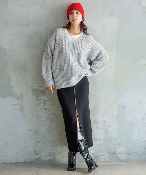 Woman in a red beanie, grey knit sweater, black skirt and patent boots