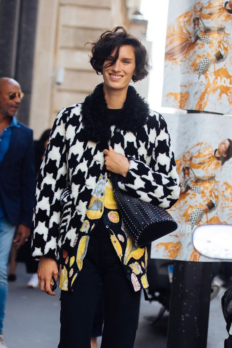 Woman in an oversized black and white houndstooth jacket with a fur collar over a colorful printed shirt