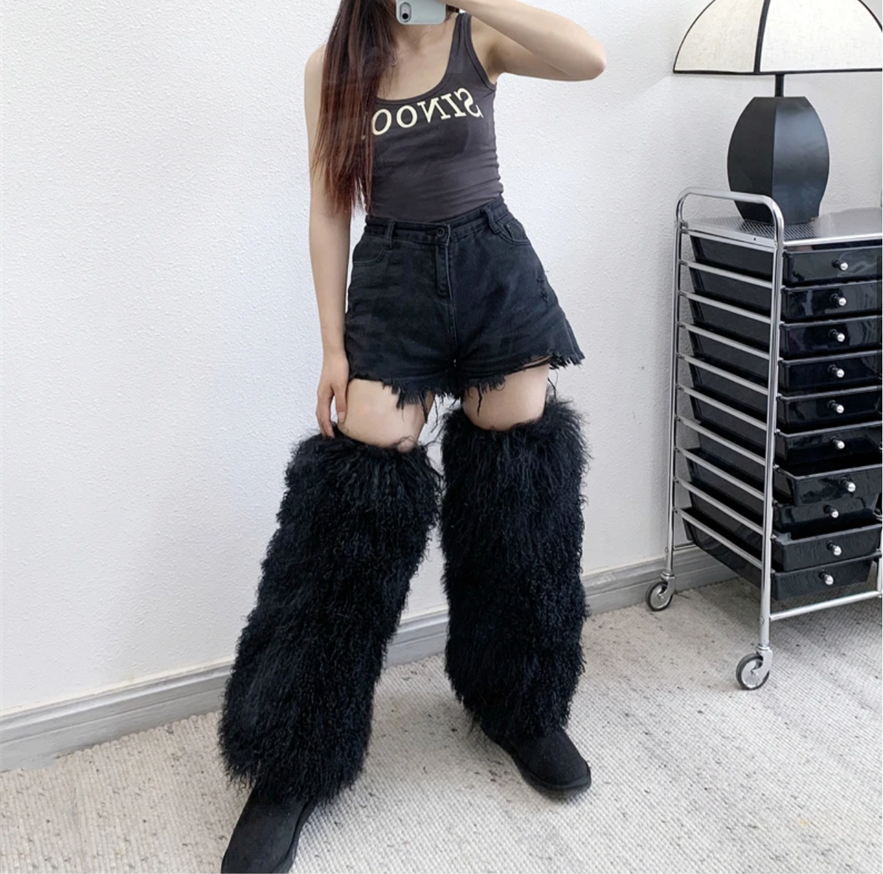 Extra long black furry leg warmers with black denim shorts and a dark tank top in a mirror selfie