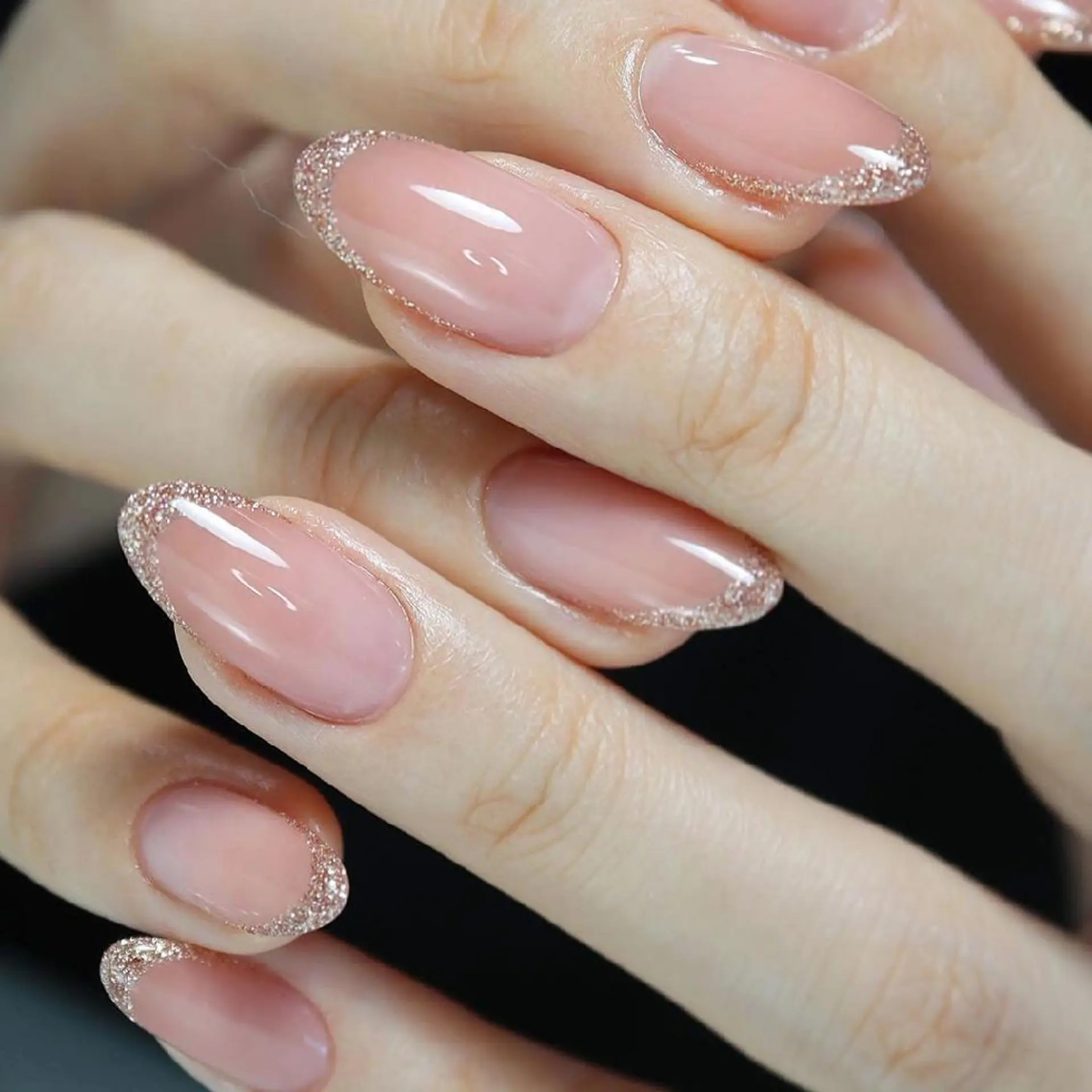 Close-up of sheer pink French manicure with gold glitter accent nails