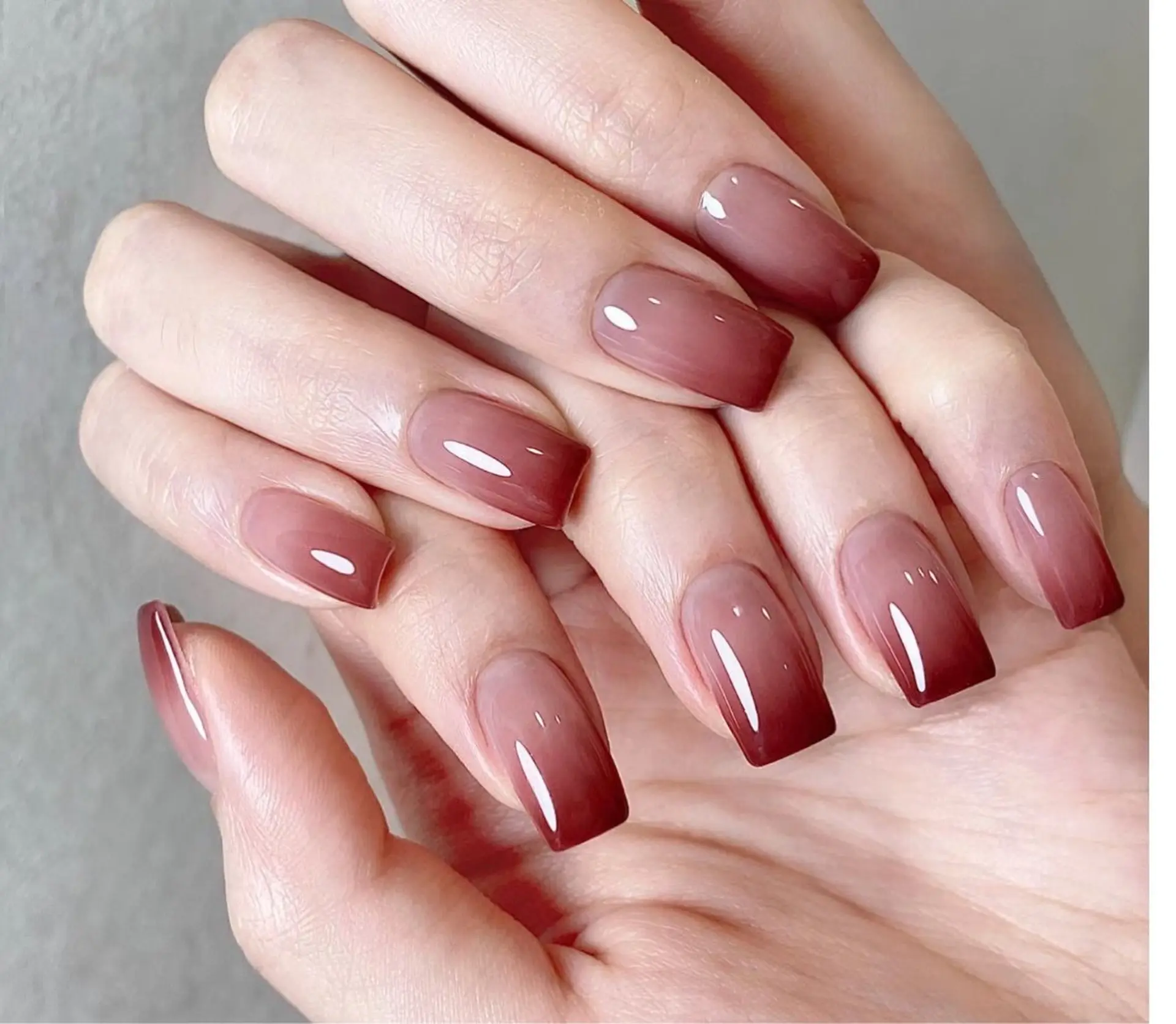 Short square nails fading from wine red to nude in a smooth ombre gradient