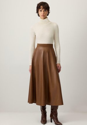 Model wearing brown leather A-line midi skirt with cream turtleneck and brown knee boots