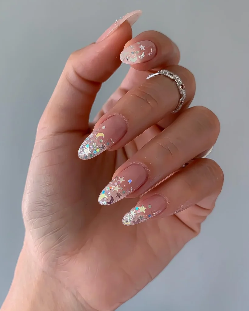 Long almond nails in sheer nude with iridescent star and moon glitter concentrated at the tips