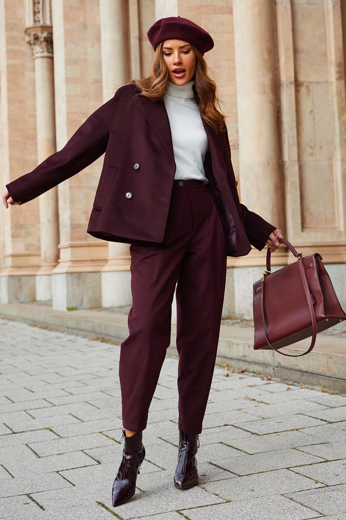 Woman wearing a burgundy peacoat, trousers, beret and ankle boots with a white turtleneck