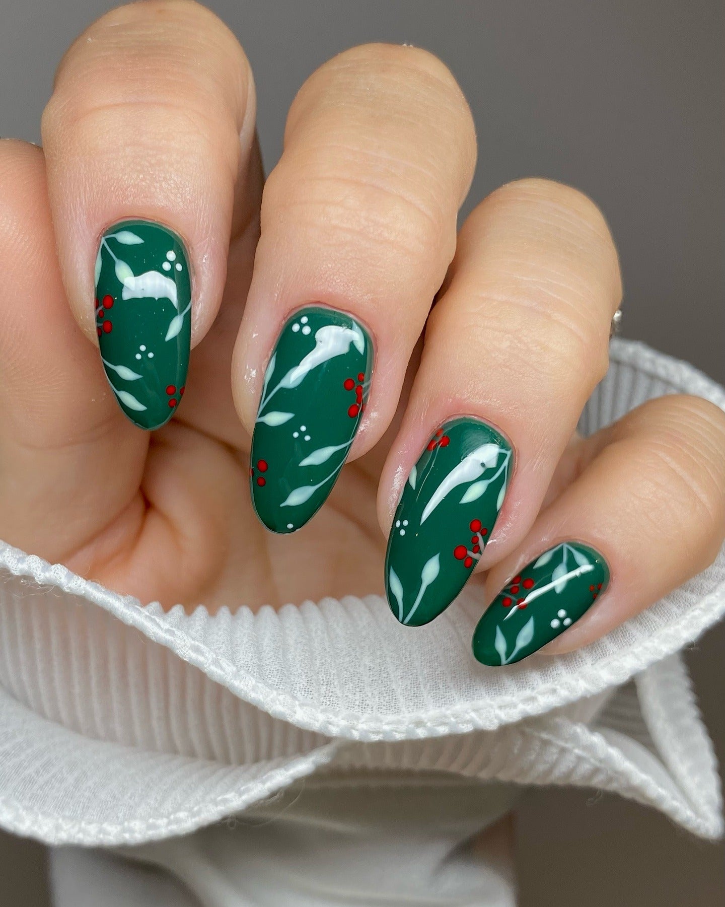 Medium almond emerald-green nails with white mistletoe leaves and red berry nail art