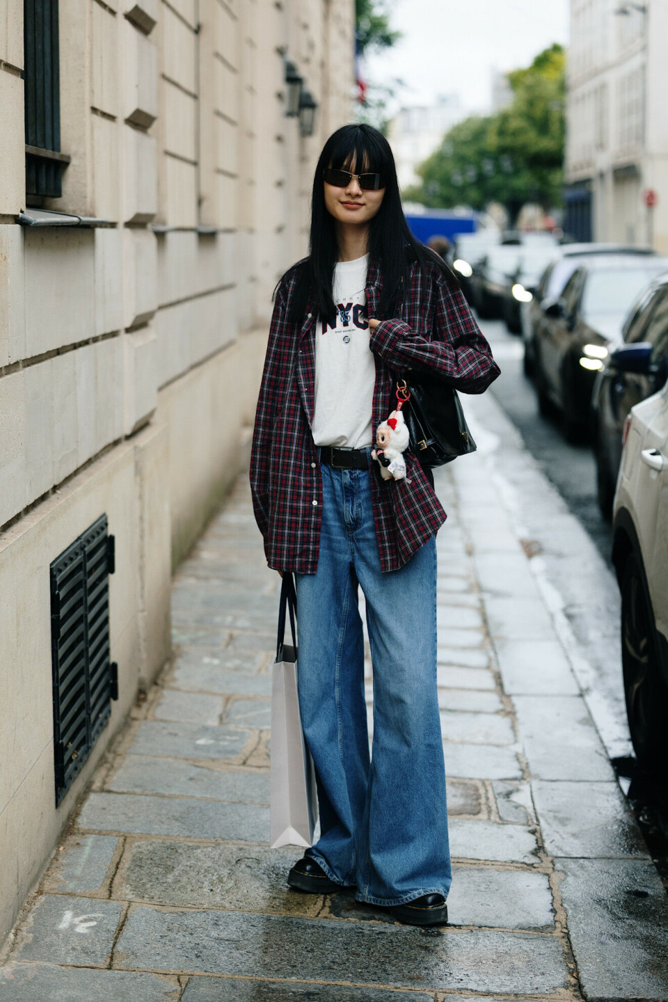Woman in an oversized red and black plaid flannel shirt, white graphic tee, wide-leg blue jeans and black platform shoes