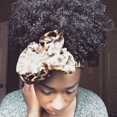Woman with natural curly hair wearing a leopard-print scarf tied as a headband