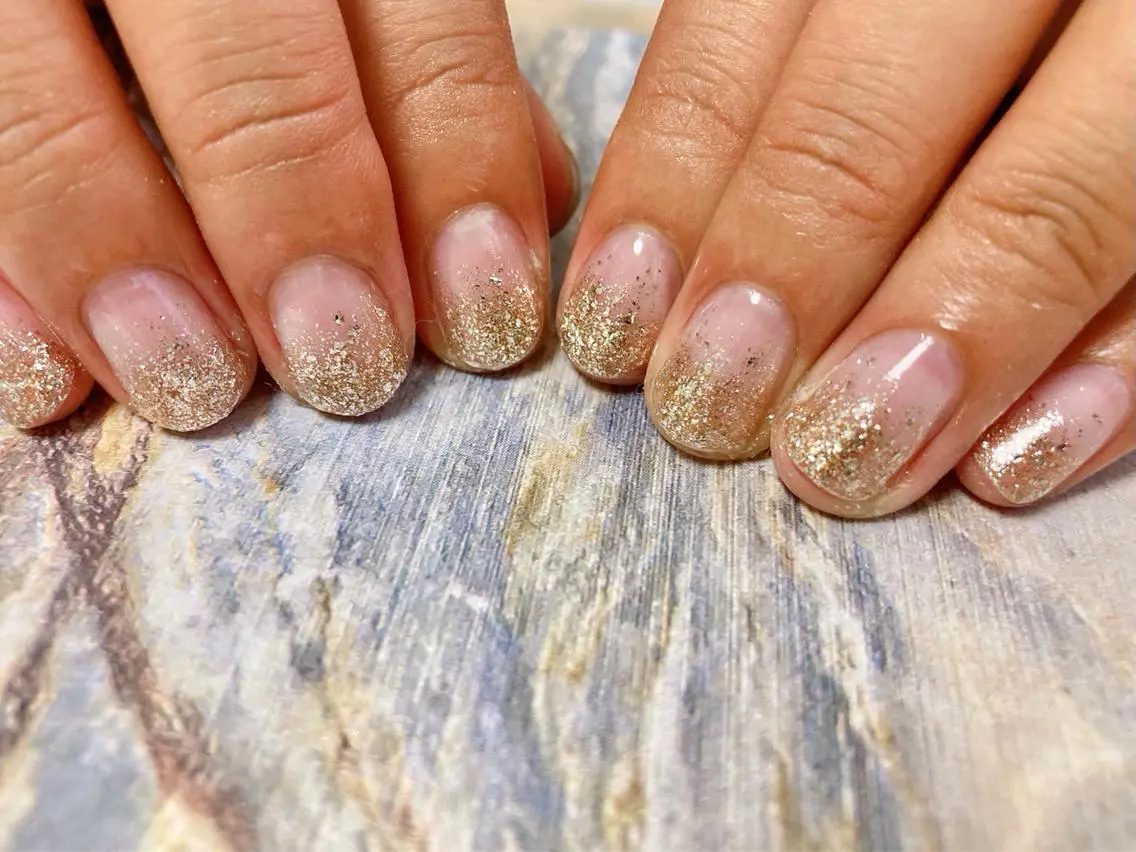 Short round nails with a pale nude base fading into champagne-gold glitter toward the tips.