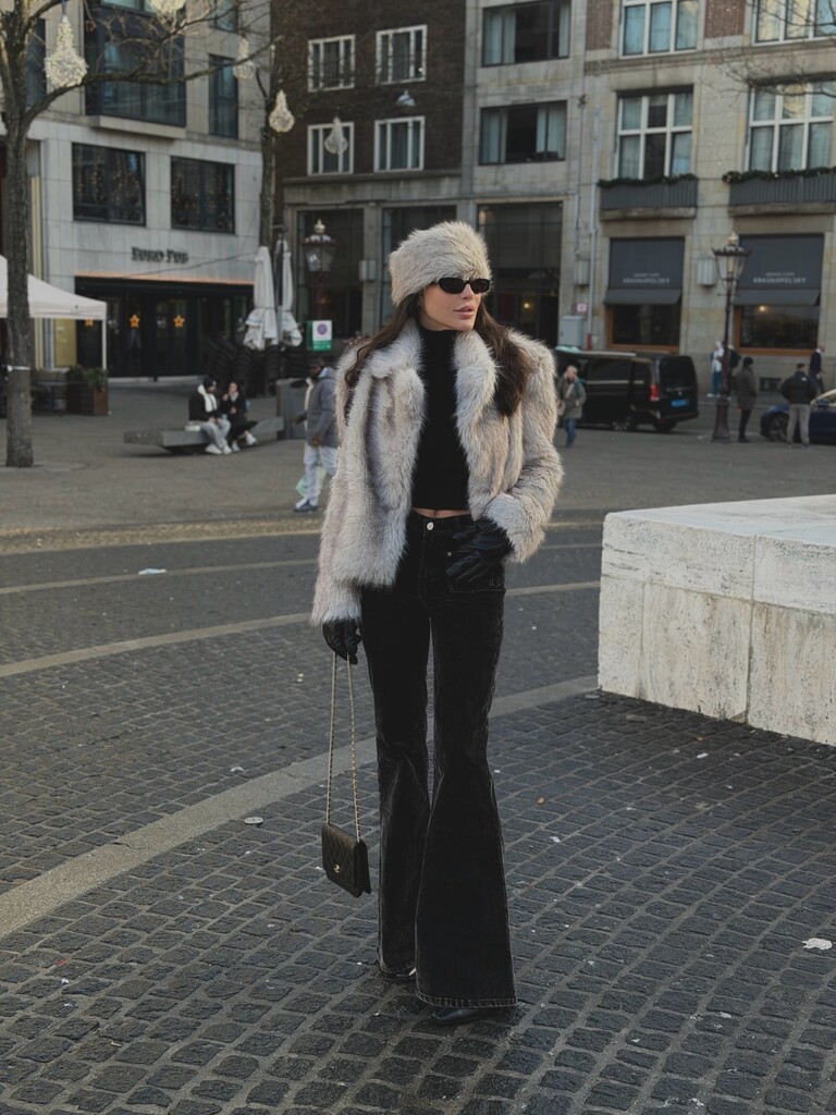 Woman in cream faux fur jacket, black turtleneck, black flared jeans and fur hat