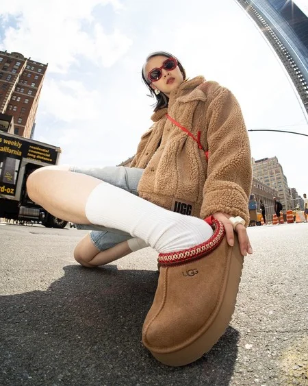 Woman wearing chestnut Ugg Tazz platform slippers with a teddy fleece jacket and white crew socks