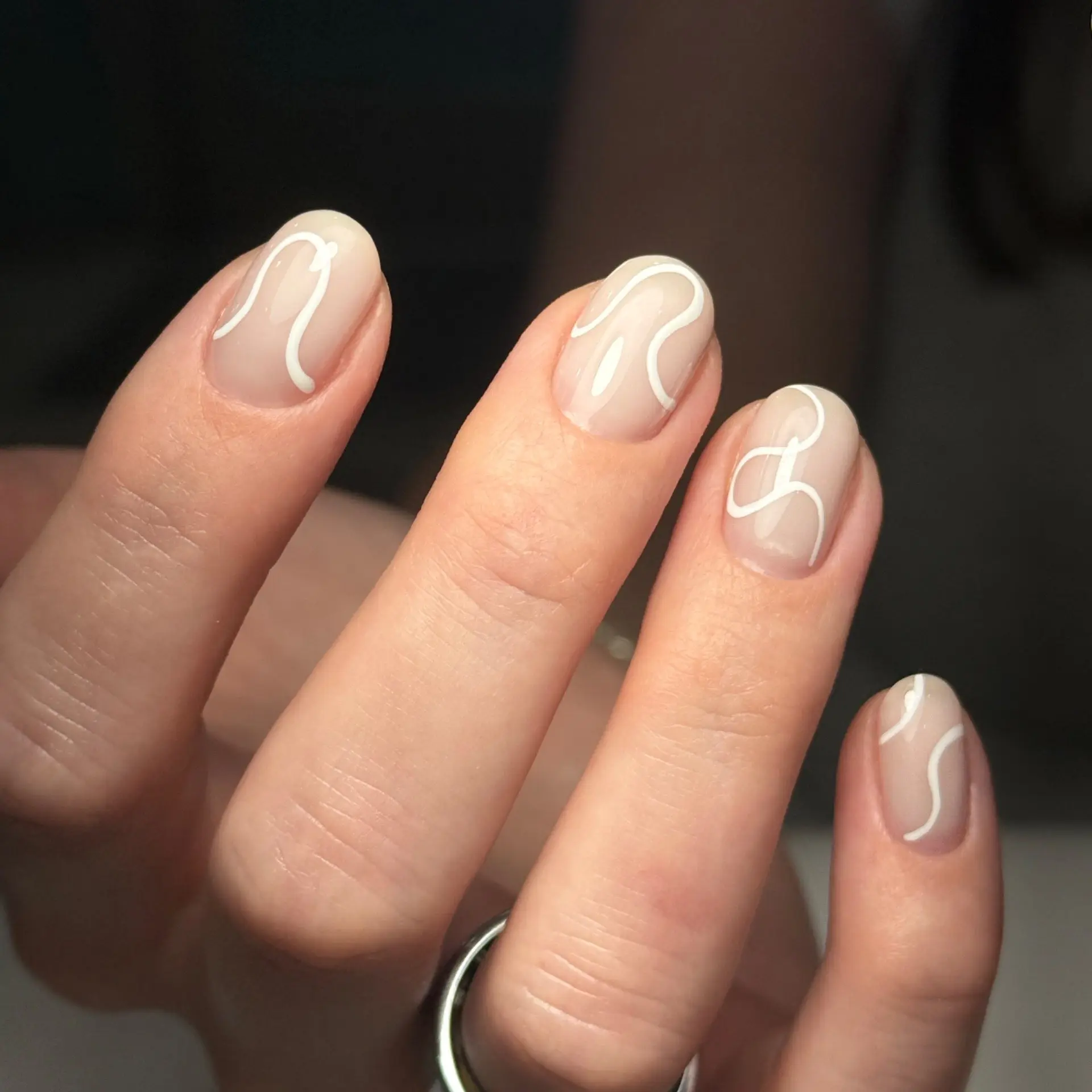 Short oval nails with sheer nude base and abstract white squiggle line art