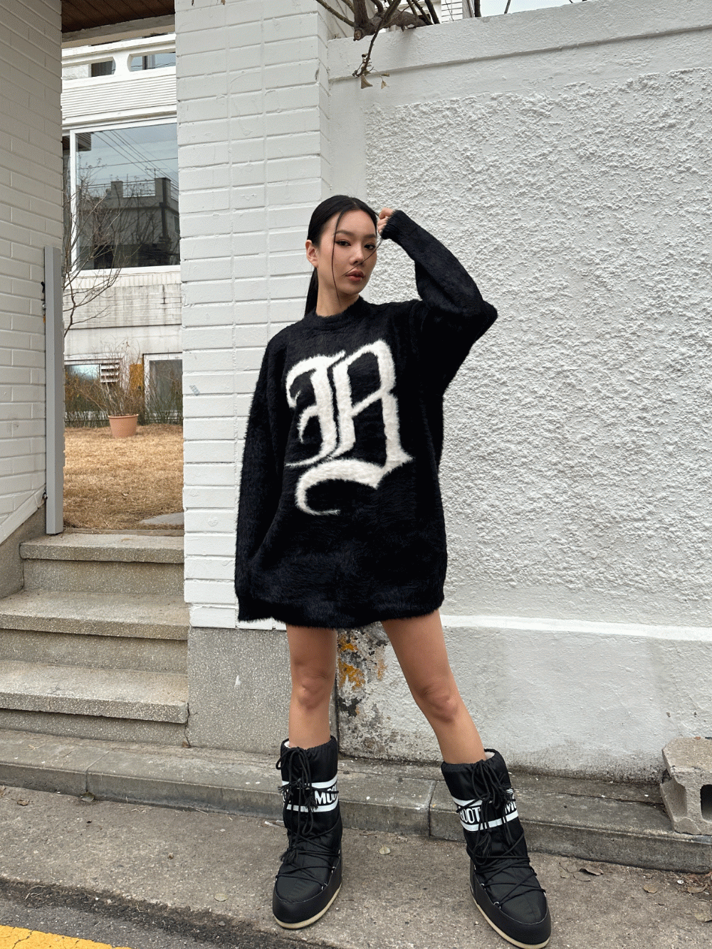Woman in black Moon Boots and an oversized black fuzzy sweater dress with white lettering