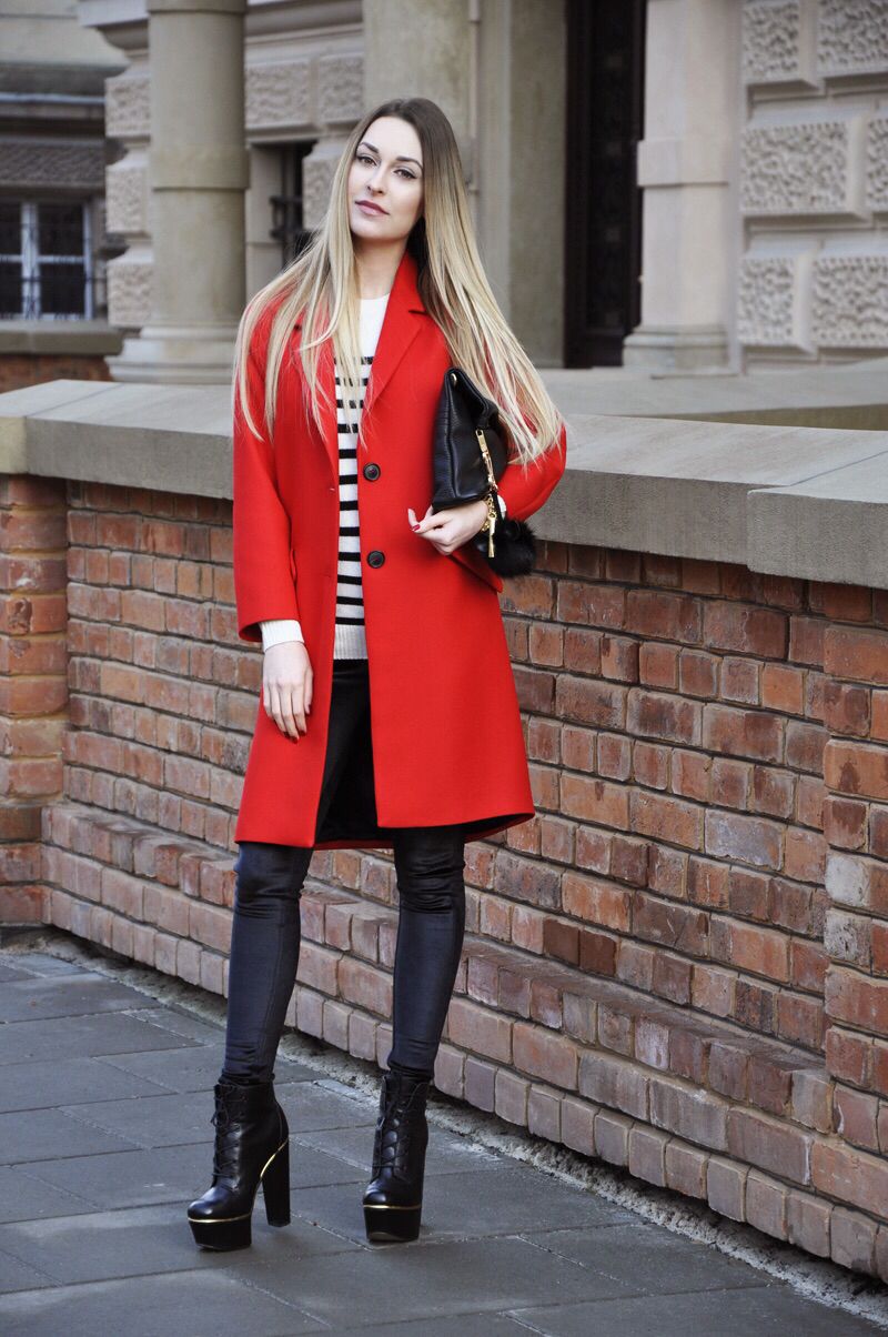 Woman in a red coat, white striped knit sweater, black leather leggings and black platform ankle boots