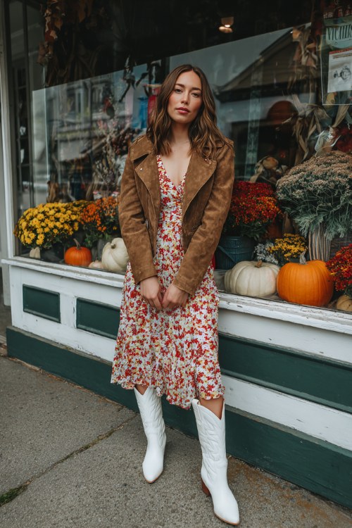 Woman wearing a red floral midi dress, tan suede moto jacket and white western ankle boots