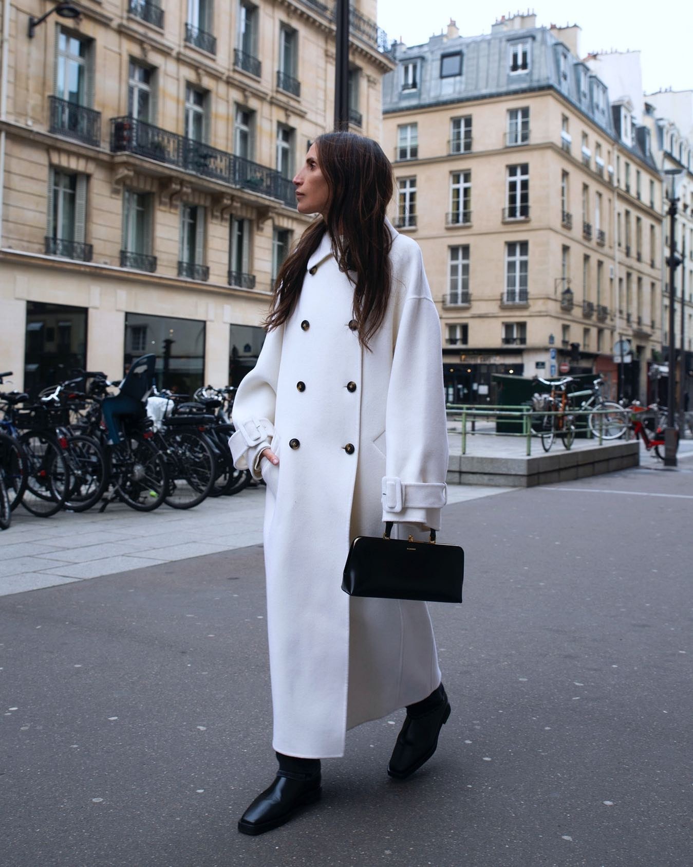 Woman in a cream double-breasted coat with black boots and a black handbag on a Paris street