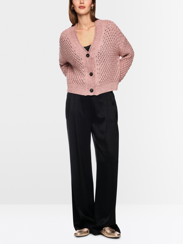Woman wearing a dusty pink open-knit cardigan with black wide-leg trousers and gold loafers