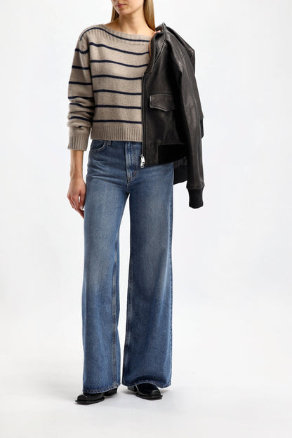 Woman in a grey striped sweater with medium-wash wide-leg jeans, a black leather jacket over her shoulders and loafers