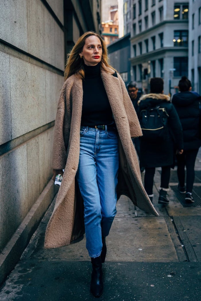 Woman in a long camel teddy coat with a black turtleneck and straight jeans on a city street