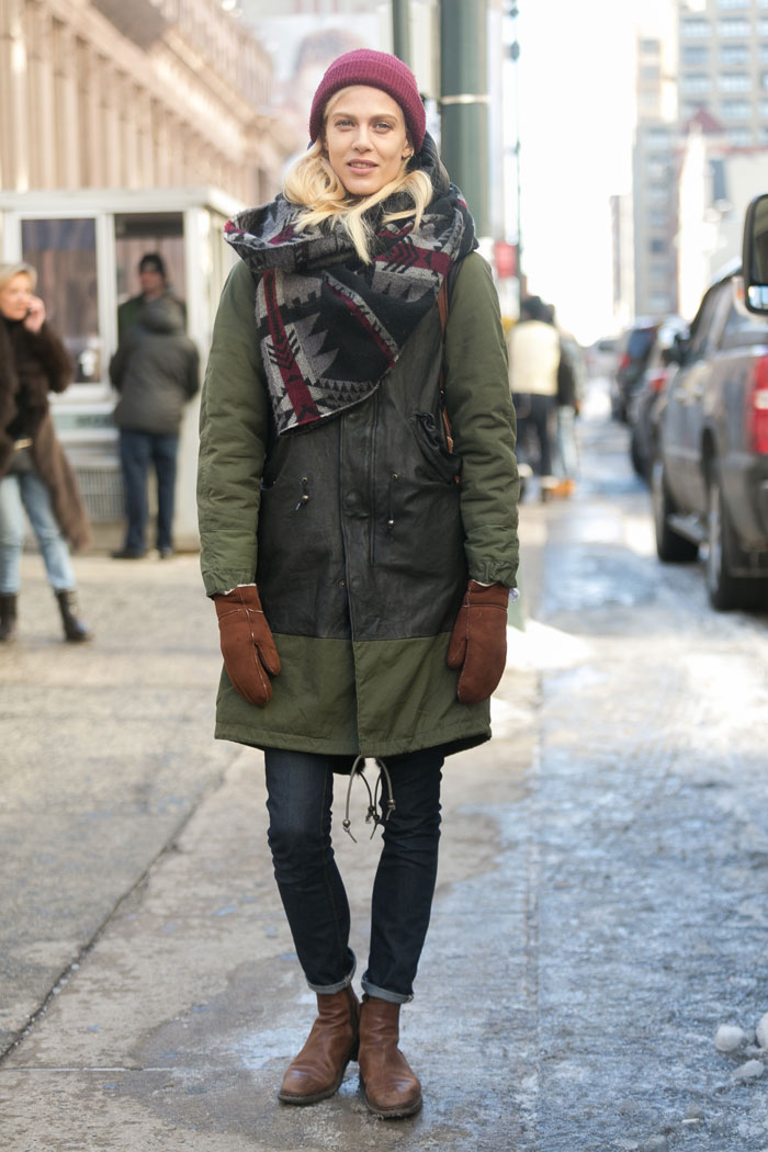 Woman in a green fishtail parka with a red beanie, patterned scarf and mittens