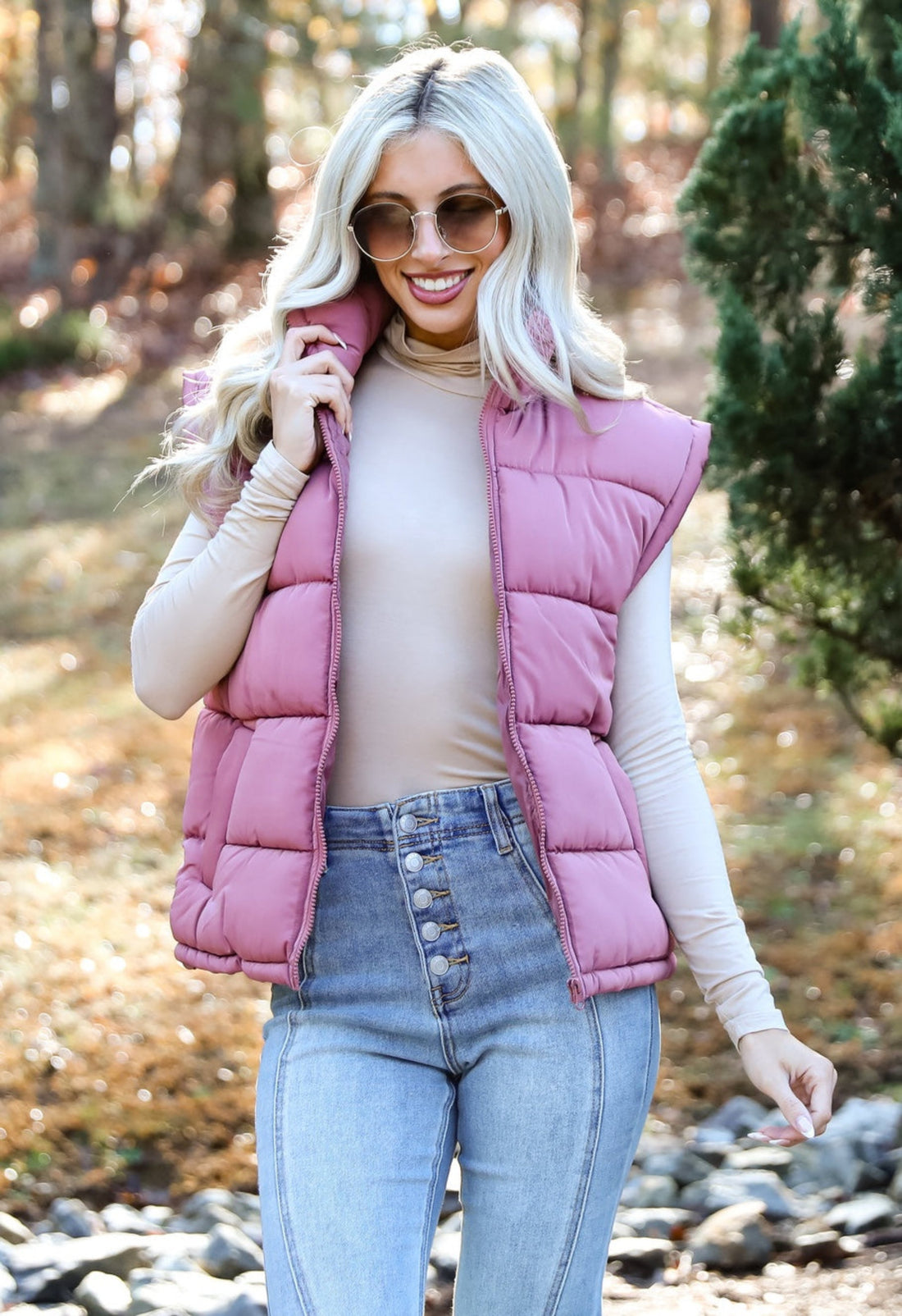 Woman wearing a nude turtleneck with a mauve puffer vest and button-fly jeans
