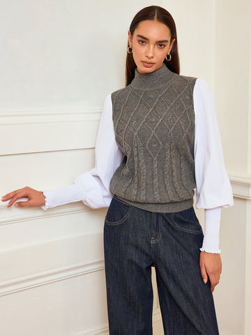 Woman in a gray cable-knit mock-neck sweater vest over a white blouse with balloon sleeves and dark wide-leg jeans