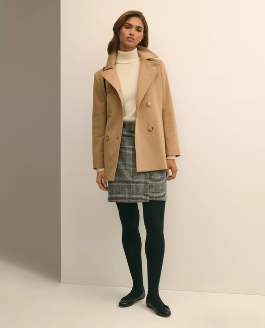 Woman in a camel double-breasted wool coat with cream turtleneck, plaid mini skirt and loafers