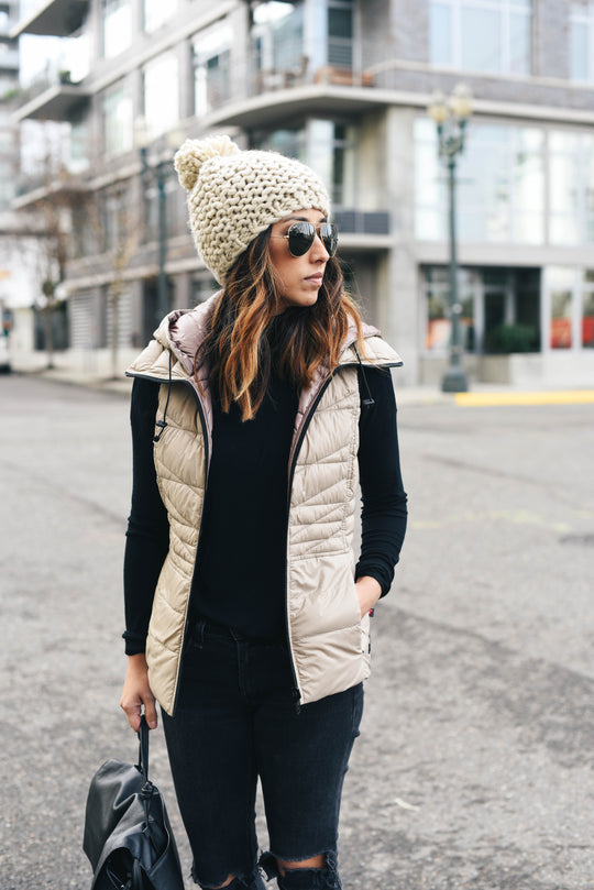 Woman wearing a quilted down vest over a black top with jeans and a knit beanie